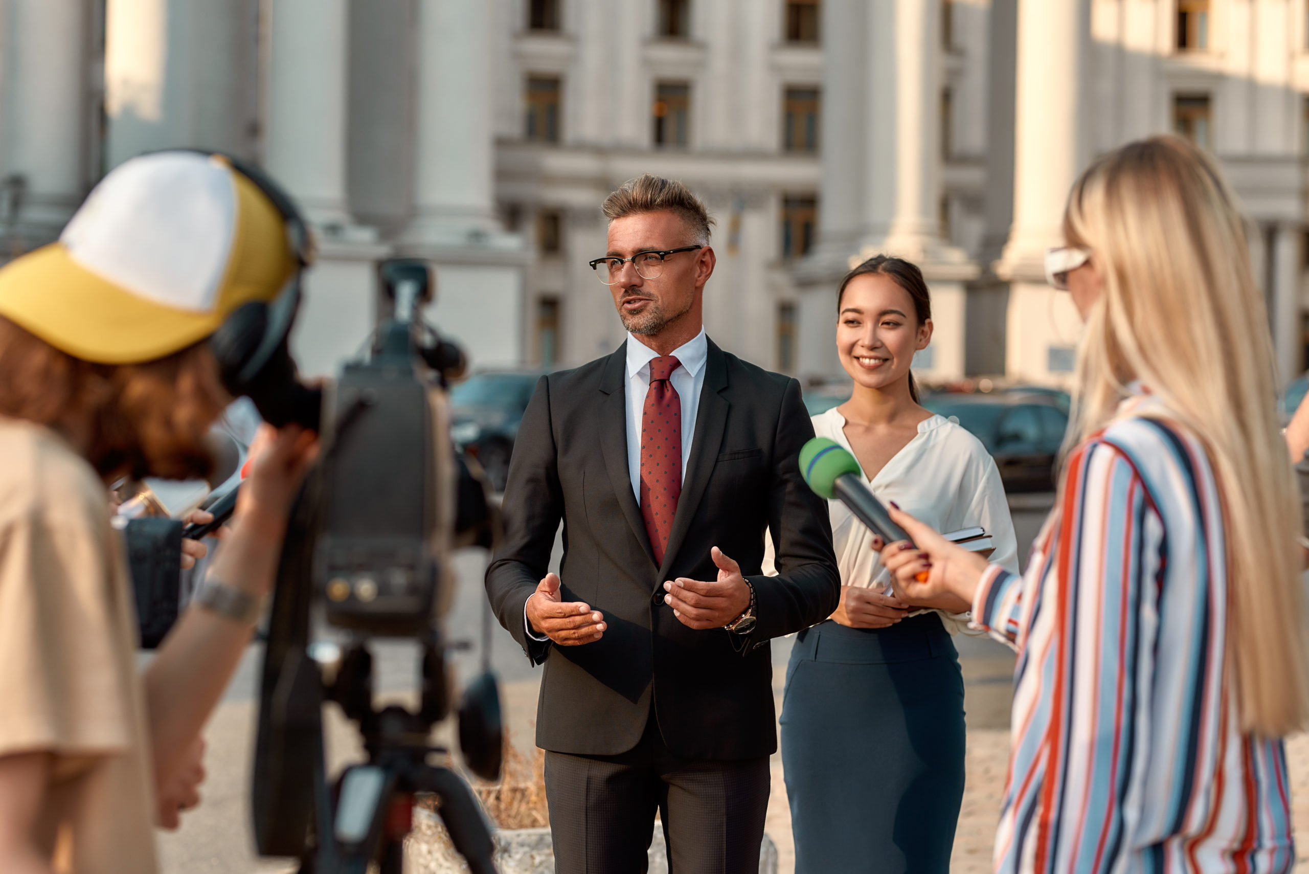 Horizontal shot of politician giving interview to journalists. People making interview using digital camera and equipment set at outdoor location. Selective focus. Front view